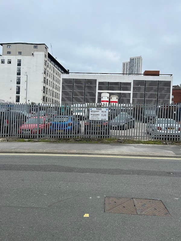 Pay & Display car park with various parked cars, surrounded by a metal fence and buildings in Leeds, Yorkshire.