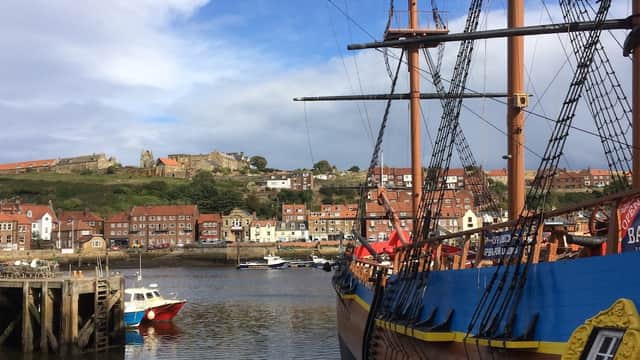 A dock with a wooden ship, colorful buildings on the hillside, and a blue sky with scattered clouds.