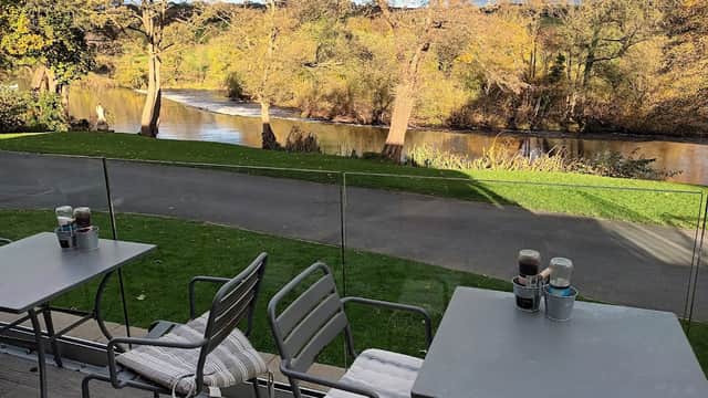 Outdoor seating at Hamiltons Cafe/Bistro overlooks a scenic river and autumn foliage in Addingham, Yorkshire.
