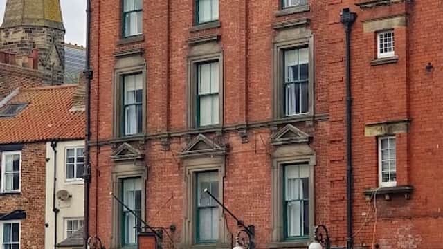 Victorian-style building with red brick facade, ornate details, and "George Hotel" sign; nearby shops and church spire visible.