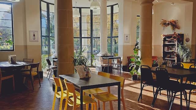 Bright event venue with large windows, wooden floors, and colorful chairs, featuring plants and cozy seating arrangements.