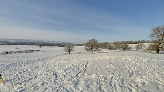 Snow-covered landscape with trees and distant hills under a clear blue sky in Weston, North Yorkshire.