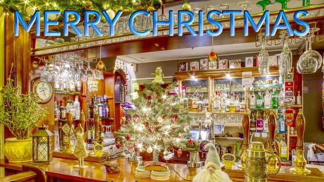 Festively decorated bar with a small Christmas tree, drinks on display, and "Merry Christmas" in bright blue letters.