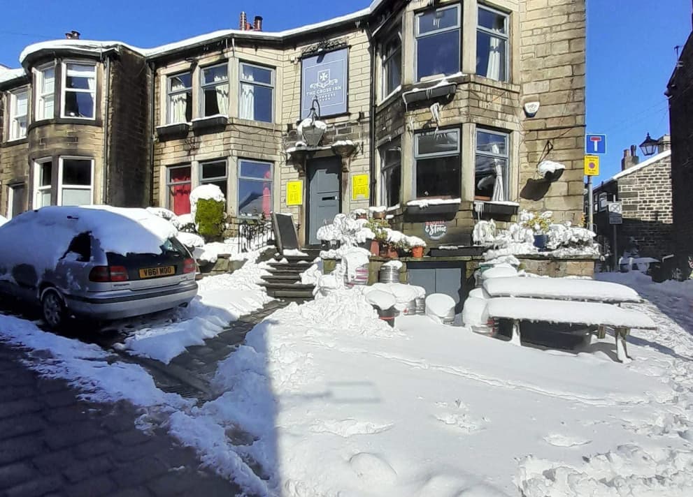 The Cross Inn bar covered in snow, with a parked car and outdoor seating visible in a winter scene.