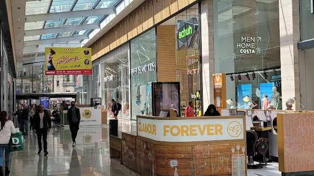Bright indoor shopping area with shops, a cafรฉ, and a skylight ceiling, bustling with people.
