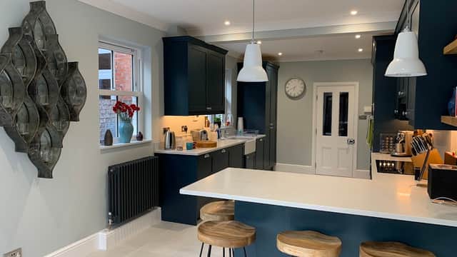 Modern kitchen with dark blue cabinets, white countertops, bar stools, and decorative wall art. Bright and spacious design.