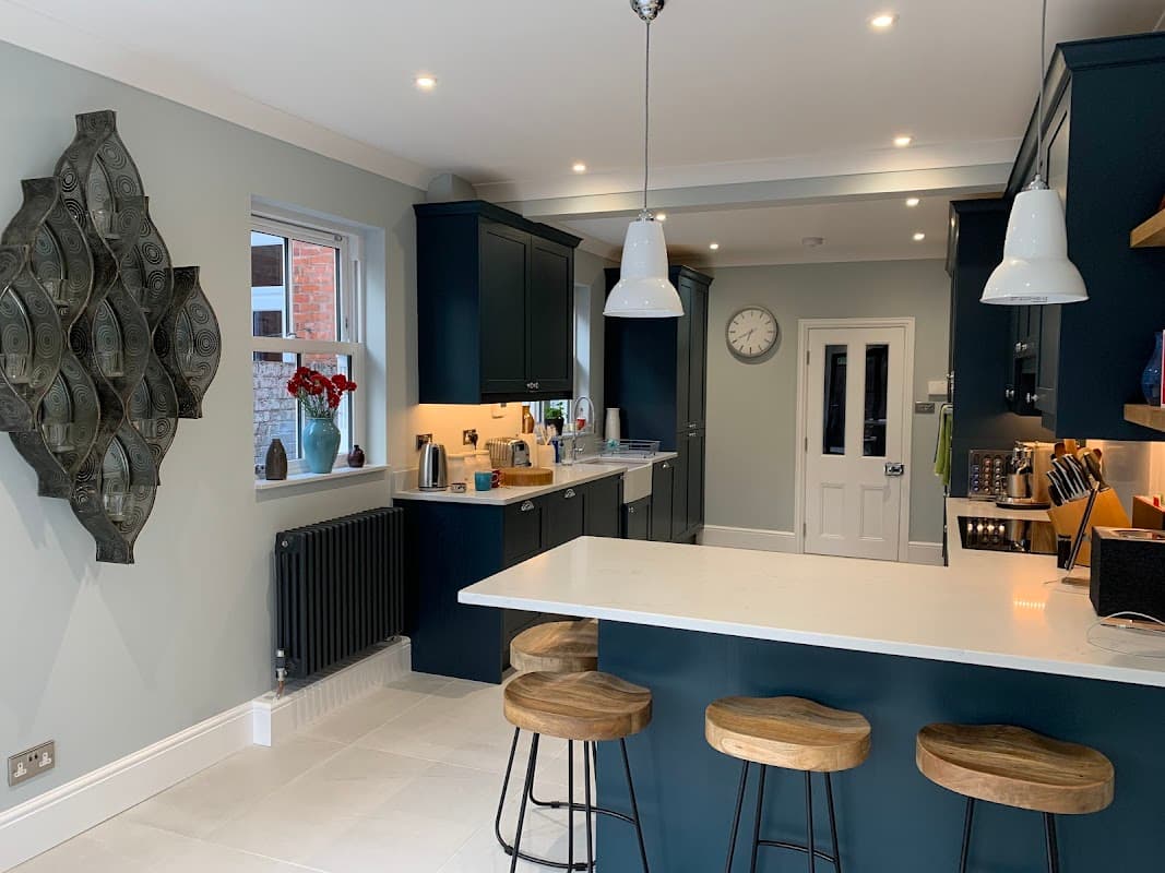 Modern kitchen with dark blue cabinets, white countertops, bar stools, and decorative wall art. Bright and spacious design.