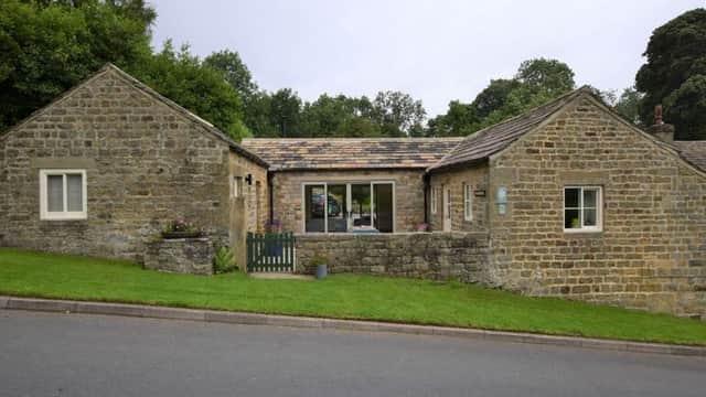 Charming stone cottage with a sloped lawn, green gate, and large windows, set in a rural North Yorkshire landscape.