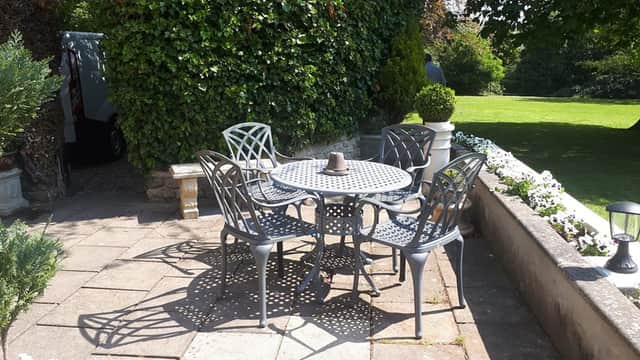 Outdoor dining area with a round table and four chairs, surrounded by greenery and a stone pathway.