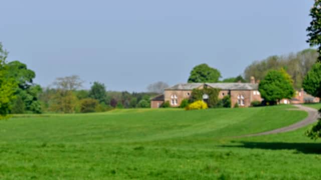 Lush green fields with a distant brick building and trees under a clear blue sky in Thornton-le-Moor, Yorkshire.