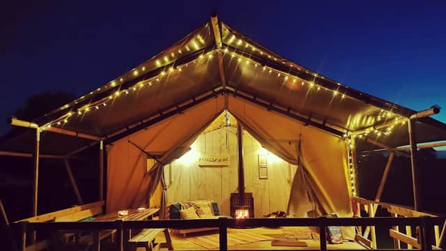 Cozy glamping tent illuminated with fairy lights, wooden deck, and peaceful evening sky at Kingfisher Lakes, Yorkshire.