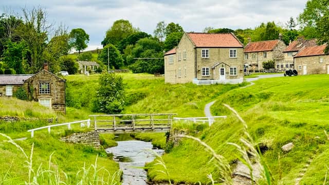 Quaint stone buildings with red roofs by a stream, surrounded by lush green fields and trees in Sinnington, Yorkshire.