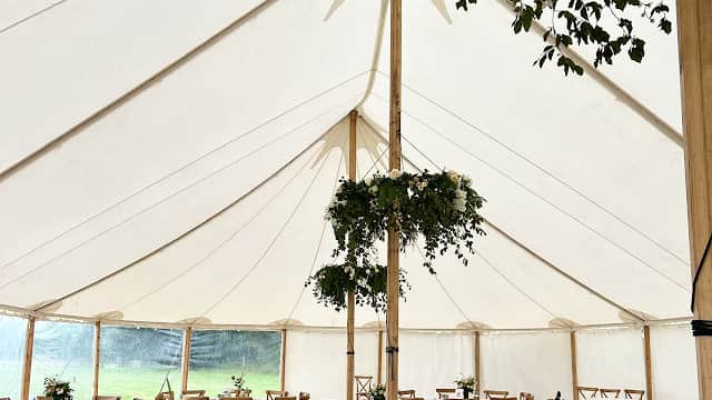 Elegant marquee with round tables, white tablecloths, and greenery hanging from the ceiling, set for an event.