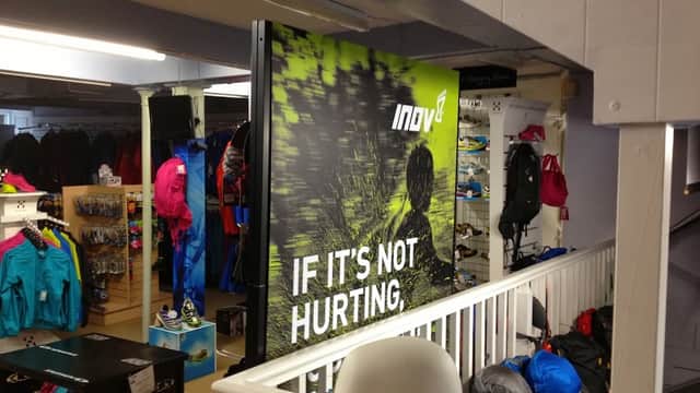 Indoor shop display at Castleberg Outdoors featuring colorful outdoor clothing and gear, with a prominent "IF IT'S NOT HURTING" sign.