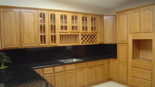 Stylish wooden kitchen cabinetry with glass-fronted upper units, a wine rack, and a sleek black countertop.