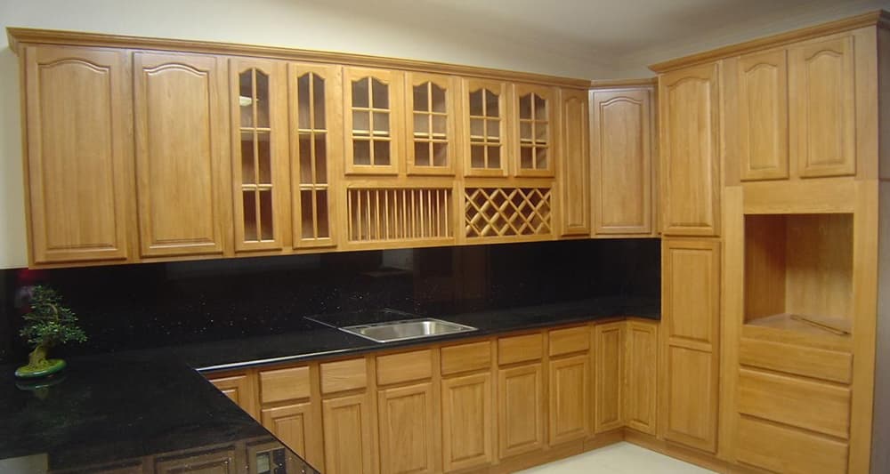 Stylish wooden kitchen cabinetry with glass-fronted upper units, a wine rack, and a sleek black countertop.