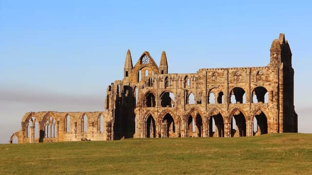 Ruins of Whitby Abbey stand against a clear blue sky, surrounded by green grass in Yorkshire.