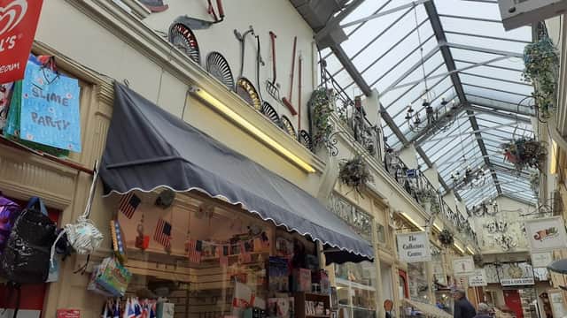 Victorian-style arcade with shops, decorative fans on walls, and a glass roof, bustling with shoppers.