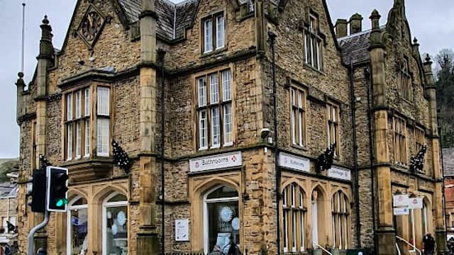 Victorian-style building with stone faΓ§ade, decorative gables, and signage for bathrooms, set in a town square.