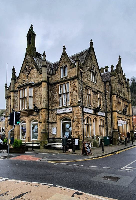Victorian-style building with stone façade, decorative gables, and signage for bathrooms, set in a town square.