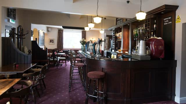 Cozy bar interior with wooden counter, stools, and a warm atmosphere, featuring drinks on display and soft lighting.