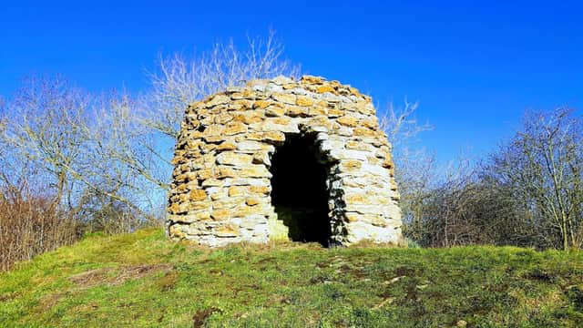 Stone structure atop a grassy mound, surrounded by bare trees under a clear blue sky.