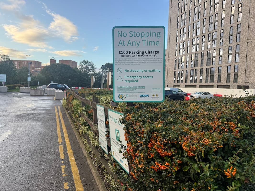 Signage detailing parking rules and charges at Whitehall Road Car Park, with shrubs and a building in the background.