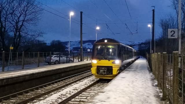Train arriving at Cononley station, snowy platform, evening lights, and trees in the background.