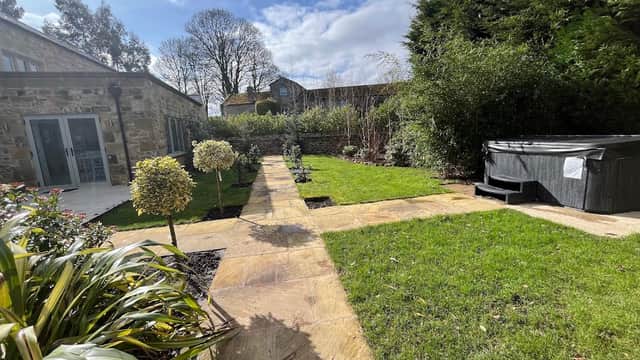 Lush garden with a stone path, hot tub, and greenery surrounding Giling Old Mill Holiday Cottages in Gilling West.