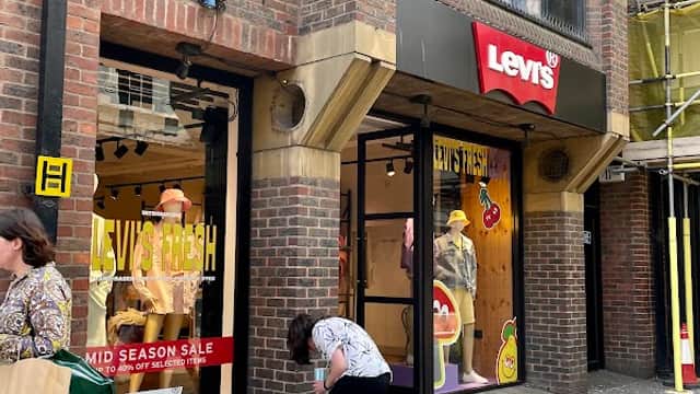 Levi's store entrance with sale signage, shoppers outside, and a person crouching by the door in York.