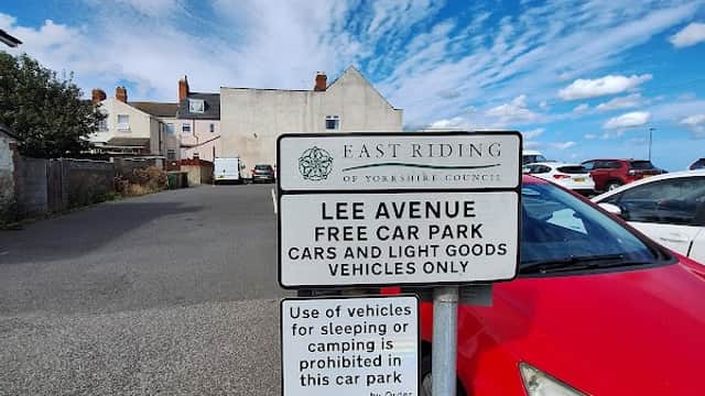 Sign for Lee Avenue Free Car Park, with a red car parked nearby and a cloudy blue sky above.