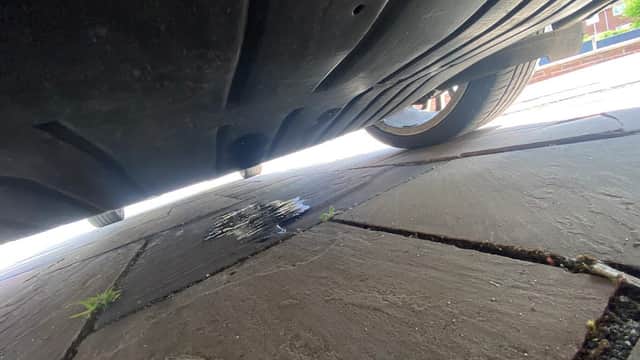 View from beneath a vehicle, showing a puddle on the stone pavement and a tire partially in the frame.