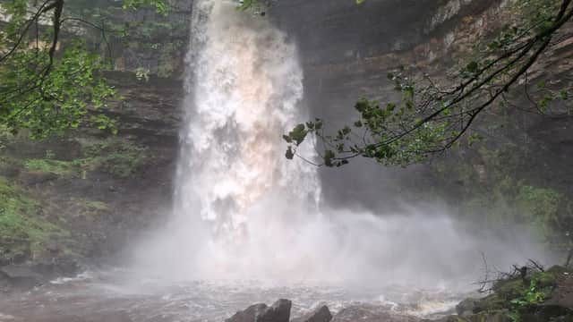 A powerful waterfall cascading over rocky cliffs, surrounded by lush greenery and mist rising from the water.