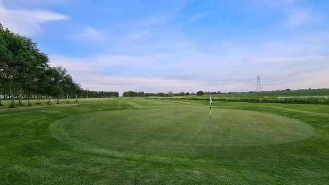 Lush green golf course with a flag on the putting green under a blue sky in Thorpe Willoughby, Yorkshire.