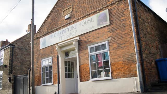 Brick building with a sign reading "The Old Picture House Pet Shop," featuring a white door and colorful window displays.