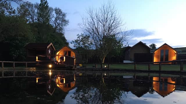Cozy wooden cabins by a tranquil pond, reflecting trees and evening sky in Bewerley, Yorkshire.