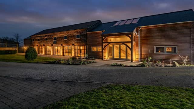 Rustic event venue with wooden exterior, large glass doors, and landscaped garden, illuminated at dusk in Kelfield.