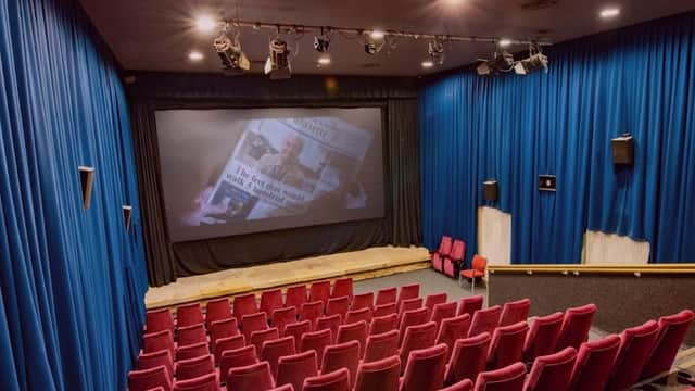 Red velvet seats facing a large screen in a cozy cinema with blue curtains and dim lighting.