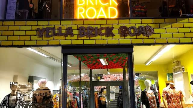 Brightly lit storefront with "YELLA BRICK ROAD" sign, colorful clothing displays, and vibrant decor.