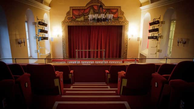 Theatrical stage with a large painted backdrop, ornate curtains, and wall sconces in a vibrant community hall.