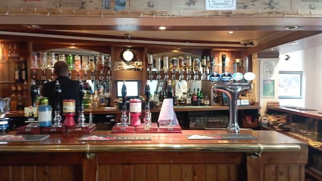 Wooden bar with various drinks, taps, and shelves of liquor; bartender serving in a cozy, rustic setting.
