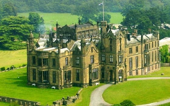 Gothic Revival castle with turrets and lush green lawn, surrounded by trees under a clear sky.