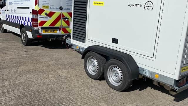 Hydroblast Limited van and a trailer-mounted pressure washer on a concrete surface under a partly cloudy sky.