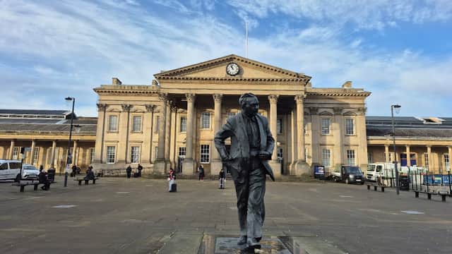 Statue in foreground with a historic building featuring columns and a clock in the background under a blue sky.