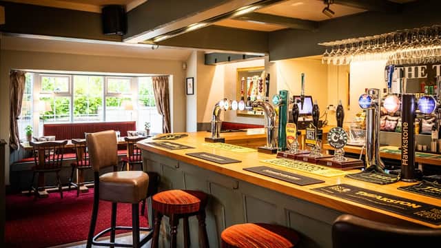 Warm interior of The Tiger Inn bar featuring wooden counter, stools, taps, and cozy seating area with natural light.