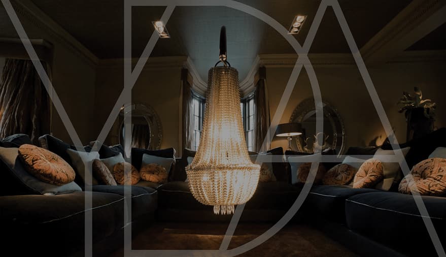 Elegant living room with a grand chandelier, plush sofas adorned with decorative cushions, and stylish lighting.