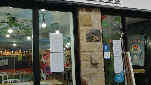 The Cake'ole café entrance with large windows, stone wall, and outdoor seating in a vibrant, welcoming atmosphere.