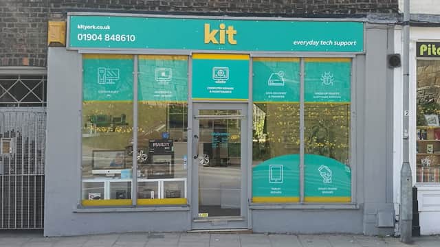 Bright storefront with "kit" signage, displaying tech support services and products behind glass windows.
