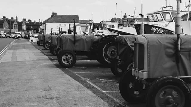 Row of covered tractors parked in Fishermans Square Car Park, with boats and buildings in the background.