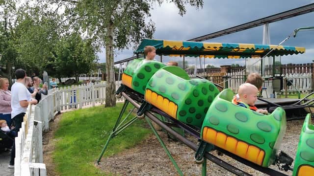 Children in green caterpillar-themed ride cars, with spectators nearby, under a cloudy sky at Flamingo Land attraction.